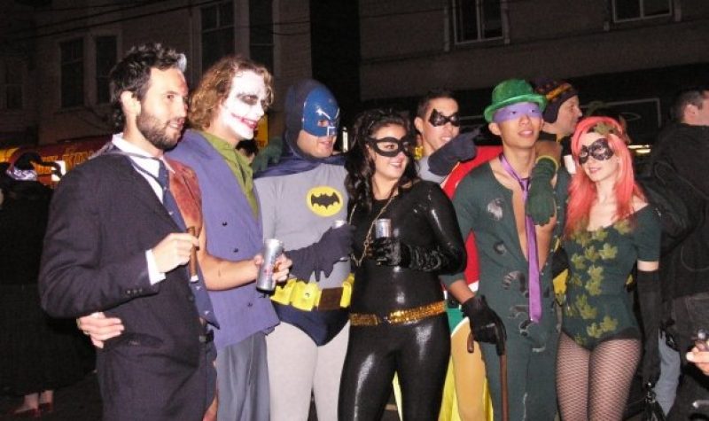 Several adults in batman themed costumes stand in a line.