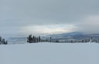 A sky view from the top of a ski mountain in Smithers BC. The sun is just breaking through the sky which is otherwise mostly clouds.