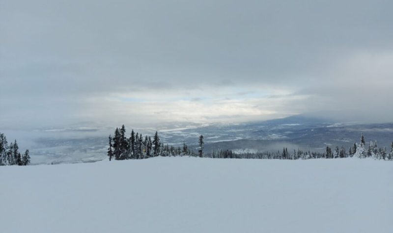 A sky view from the top of a ski mountain in Smithers BC. The sun is just breaking through the sky which is otherwise mostly clouds.