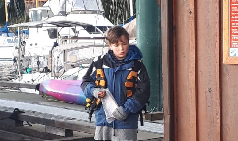 Youth in life jacket walks on dock with yacht in background