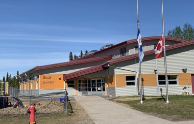 Face d'une école, sous un ciel bleu, drapeaux des T.N.-O. et du Canada en berne.