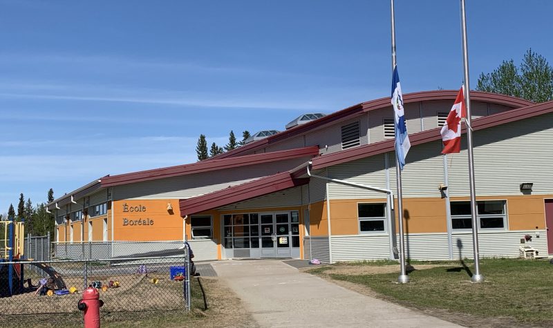 l'entrée d'une école en été. Les drapeaux des TNO et du Canada sont en berne.