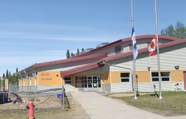 En été, la devanture d'une école. Les drapeaux du Canada et des Territoires du Nord-Ouest sont en berne.