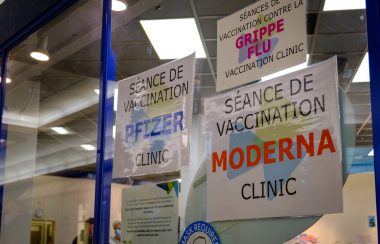 Sur une baie vitrée, trois affichent annoncent le vaccin Pfizer, le vaccin contre la grippe et le vaccin moderna