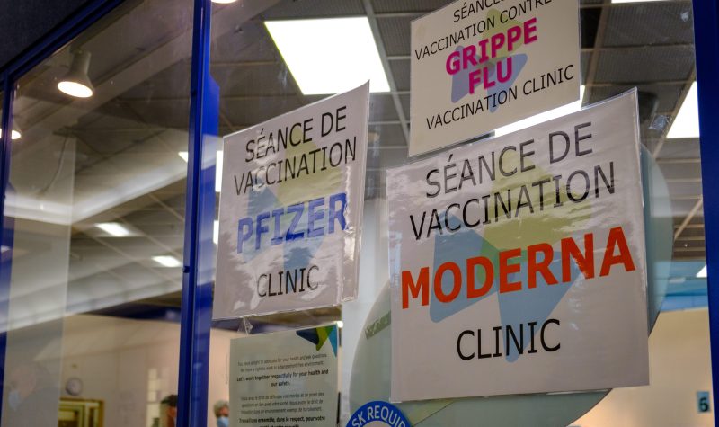 Sur une baie vitrée, trois affichent annoncent le vaccin Pfizer, le vaccin contre la grippe et le vaccin moderna