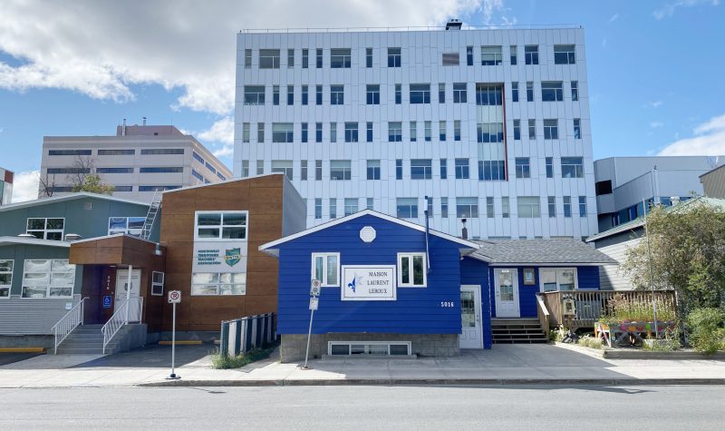 Une petite maison bleue se dresse devant un édifice de six étages.