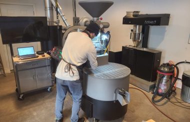 A man is facing a very large coffee bean roaster that he is working to roast beans.