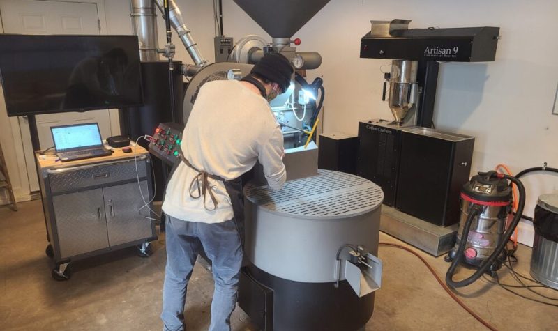 A man is facing a very large coffee bean roaster that he is working to roast beans.