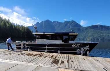 A man on a dock is pulling on a rope attached to a black boat.