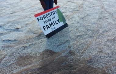 A sign rests against the legs of a protester that reads 'Forestry Feeds My Family'