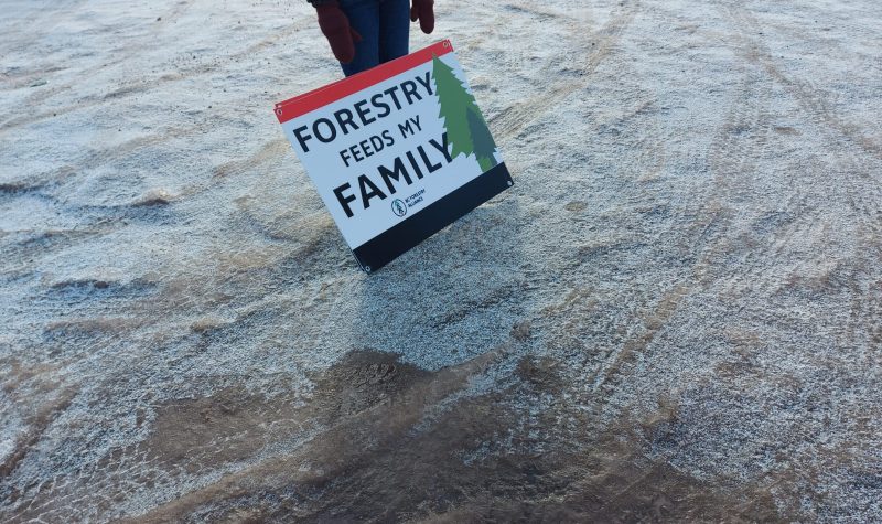 A sign rests against the legs of a protester that reads 'Forestry Feeds My Family'