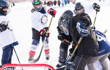 Kids on the ice of Chestermere Lake, beginning a face off in a game of hockey. Weather conditions are fair.