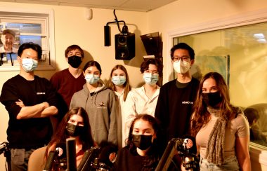 Un groupe de neuf jeunes avec couvres visages, posent pour une photo dans un studio de radio.