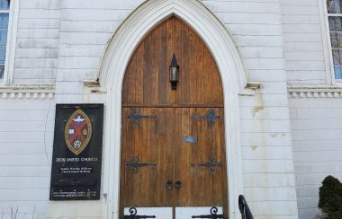 The wooden front door of a white church