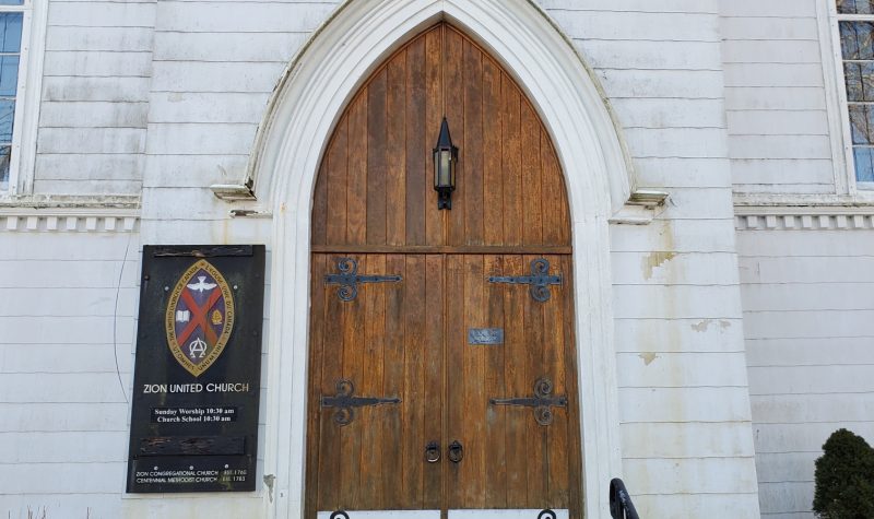 The wooden front door of a white church