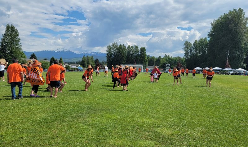 People in orange shirts dance traditionally on a soccer field