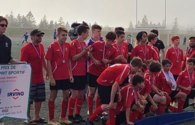 Une vingtaine de jeunes joueurs de soccer, vêtus de maillots rouges et avec une médaille au cou, recevant la bannière de l'esprit d'équipe.