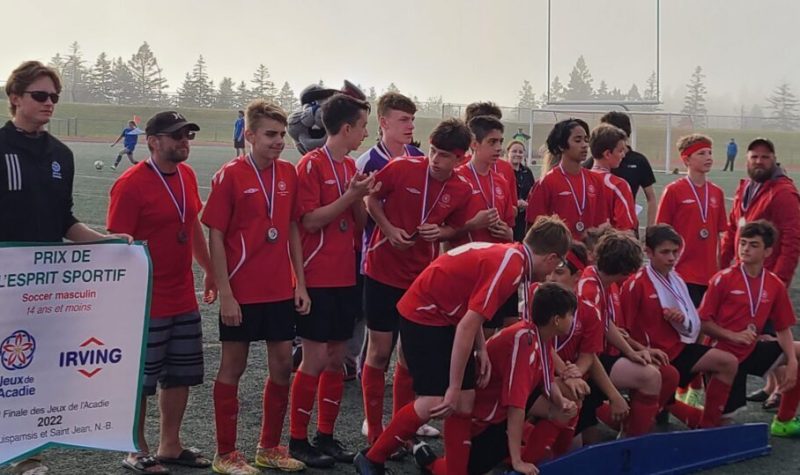 Une vingtaine de jeunes joueurs de soccer, vêtus de maillots rouges et avec une médaille au cou, recevant la bannière de l'esprit d'équipe.