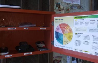 An orange box on a public wall, with the door ajar, revealing free naloxone kits, and condoms.