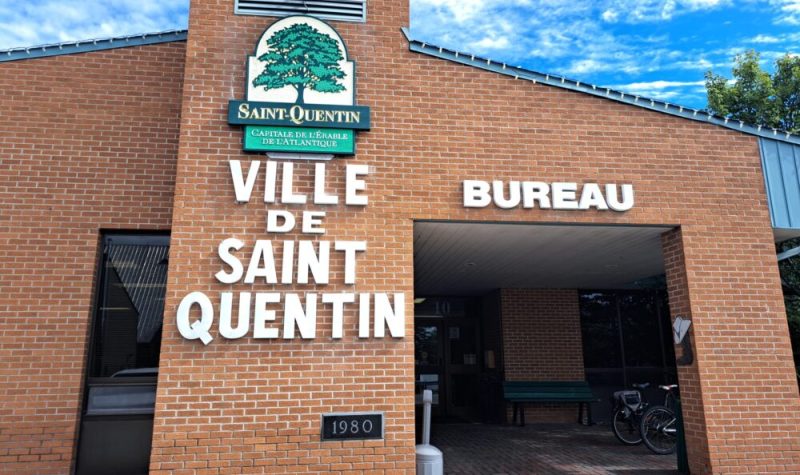 Édifice municipale en briques indiqué en lettre Ville de Saint-Quentin avec le logo de la Ville en haut des lettres. en haut de l'édifice il y a un ciel bleu avec des nuages