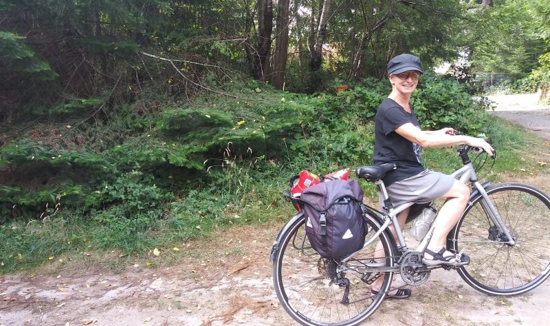 A woman stands with her bike, equipped with panniers.