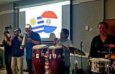 El grupo de Música la Banda Loca tocan delante de las banderas de Uruguay y Paraguay