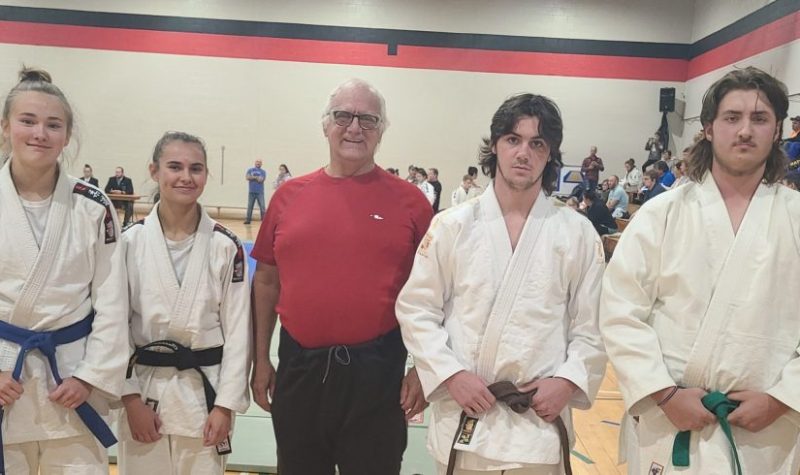 4 judokas avec au milieu un homme au gilet rouge, lors d'une compétition de Judo à l'intérieur d'un gymnase