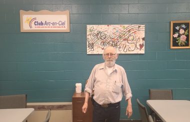 Le president du club des ainés pose dans une des nouvelles salles du club. Mur bleu, logo du club accroché au mur.