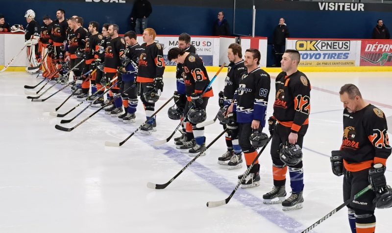 Des joueurs de hockey en uniforme foncé sont alignés sur la ligne bleue d''une patinoire à l'intérieur d'un aréna