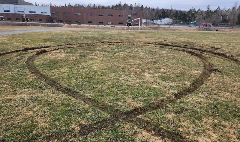 On peut voir les traces de pneus et de freinage dans le gazon du terrain de soccer, en arrière plan le centre scolaire.