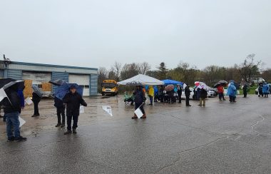 Bus drivers on strike picket in the rain outside of a blue garage.