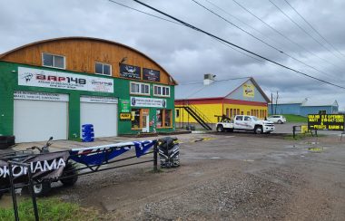 The exterior of auto shop BQP 148, with a green exterior and two white garage doors.