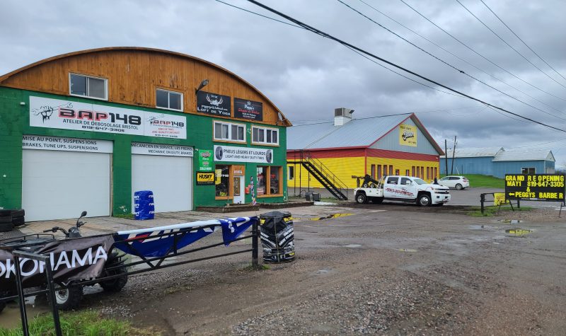 The exterior of auto shop BQP 148, with a green exterior and two white garage doors.