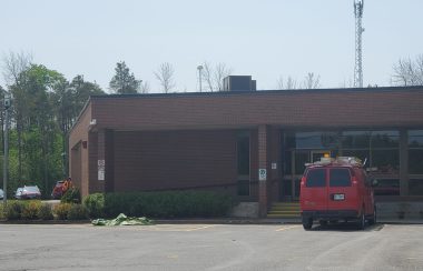 Municipal building in background with red township van parked in front and more vehicles to left hand side.