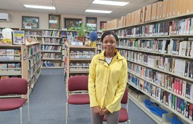 Camile Kuate vêtu d'un manteau jaune à l'intérieur de la Bibliothèque publique de Kedgwick.