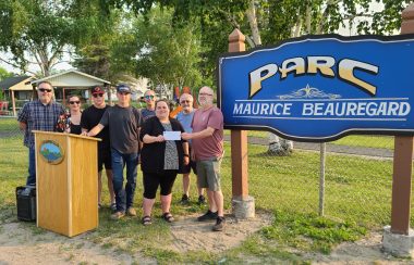 A group of people stand near a sign for Maurice Beauregard Park while a cheque is presented.
