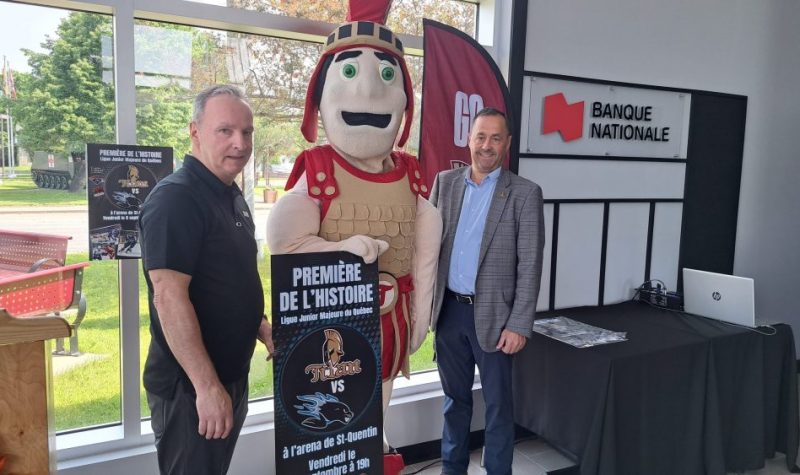 Deux hommes aux côtés de la mascotte du Titan d'Acadie Bathurst au Palais Centre-Ville de Saint-Quentin