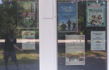 A window full of event posters casts a reflection of a man showing off the lineup.