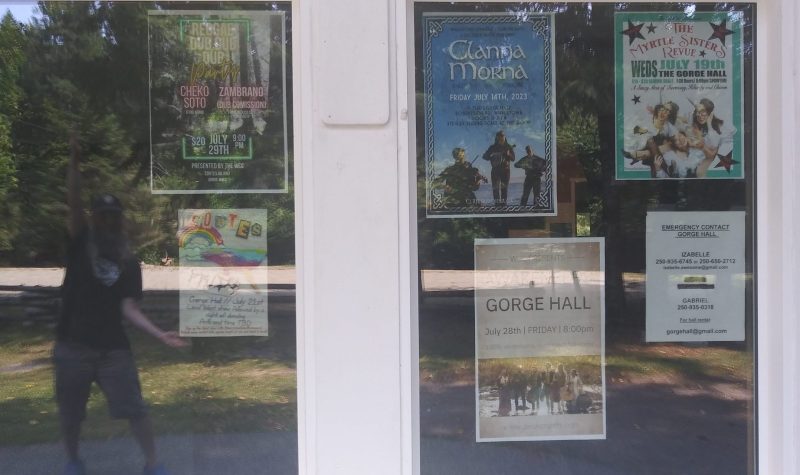 A window full of event posters casts a reflection of a man showing off the lineup.