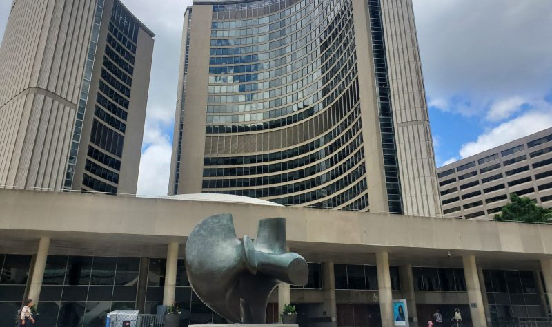 Toronto city hall with partial clouds in the background and a statue in the foreground