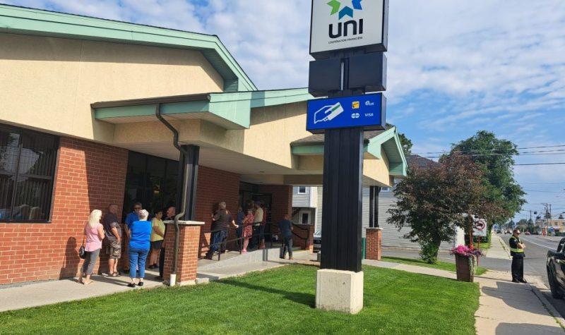 Une file d'attente d'une quinzaine de personnes devant l'UNI Coopération financière de Saint-Quentin, lors d'une journée ensoleillée.