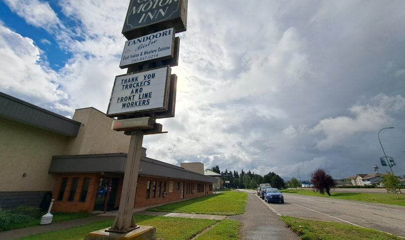 A hotel sign says The Capri Motor Inn. A one storey building is behind the sign along a frontage road in Smithers, BC.