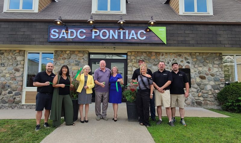 A group of people standing outside a stone building with three dormers and a sign that says SADC Pontiac.