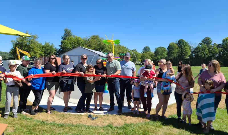 A group of people standing in line cut a red ribbon in front of a splash pad