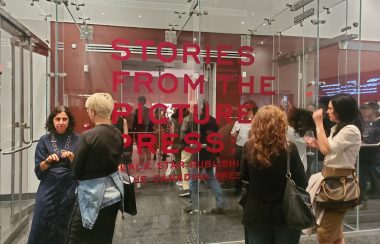 Four people standing in front of a glass screen with 'Stories From the Picture Press' written on the window in red vinyl