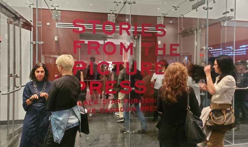 Four people standing in front of a glass screen with 'Stories From the Picture Press' written on the window in red vinyl