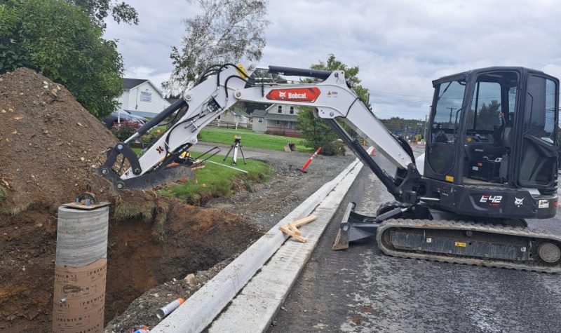 Une excavatrice blanche et noire dans un chantier de travaux routier lors d'une journée nuageuse