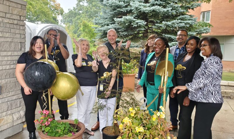 A group of people behind three potted plants clapping while one holds a golden shovel
