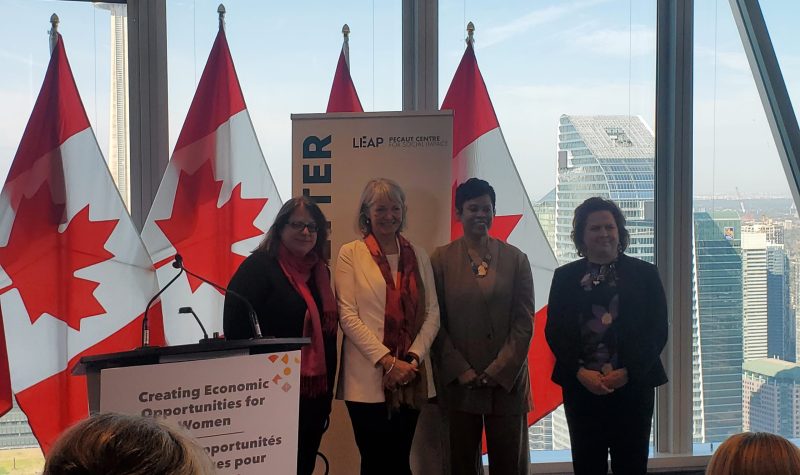 Four women standing in front of Canadian flags with the Toronto skyline behind them