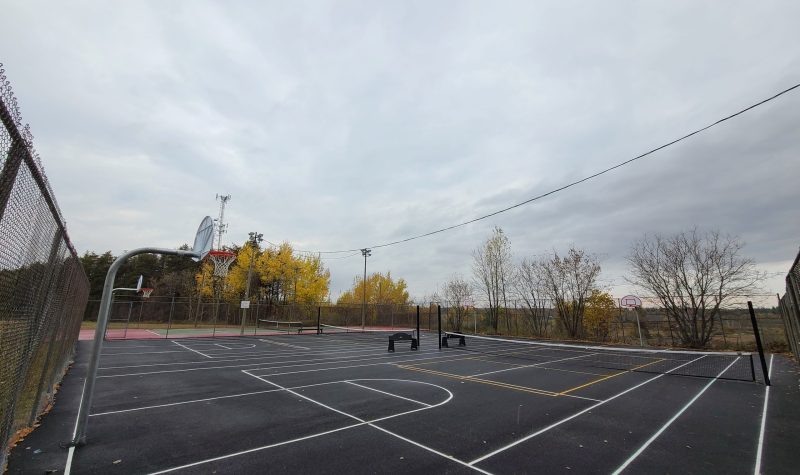 A freshly asphalted outdoor court with basketball and pickleball nets.